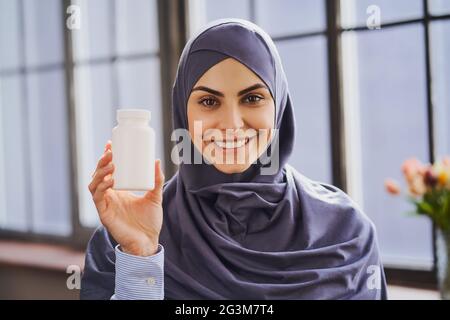 Allegra donna musulmana che tiene una bottiglia di pillole e dà un ampio sorriso Foto Stock
