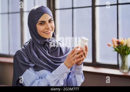 Donna musulmana felice che tiene una bottiglia di pillole e che dà un sorriso sincero Foto Stock