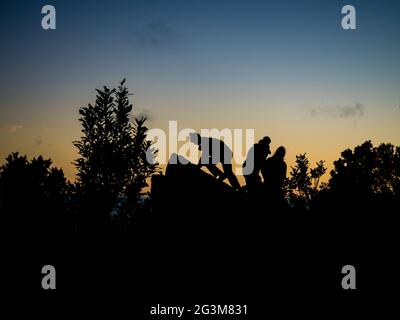 silhouette di appassionati escursionisti si siedono su una roccia per guardare l'alba Foto Stock