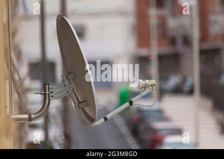 Antenna satellitare bianca installata sulla facciata di un edificio in una città. L'antenna è a fuoco e la strada è fuori fuoco in background Foto Stock