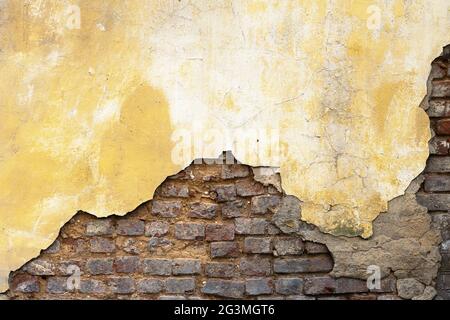 Sfondo un vecchio muro con gesso sbriciolato dipinto con una vernice arancione e mattoni rossi esposti Foto Stock