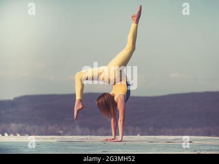 Bella donna atletica si allunga e fa un ponte sullo sfondo del cielo. Foto Stock