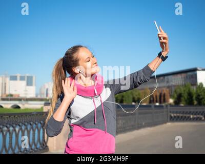 Una giovane donna prende un selfie usando uno smartphone mentre fa jogging al mattino. Il concetto di uno stile di vita sano e di mantenersi in forma. Foto Stock