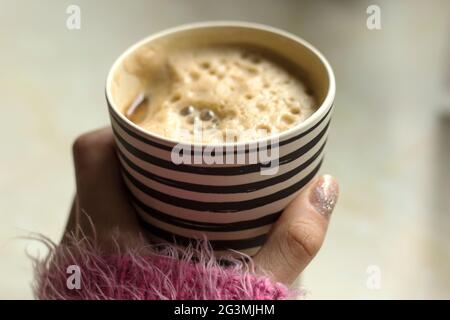 La donna sta tenendo una tazza di viaggio di bambù con caffè schiumoso e latte di soia/soia. Tazza di caffè Stripey sul banco Foto Stock