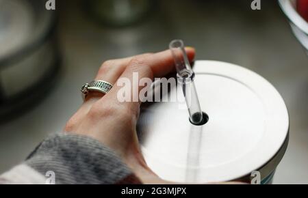 Tenendo a mano una cannuccia trasparente di un thermos d'argento in acciaio inossidabile. Tazza da caffè da viaggio Foto Stock