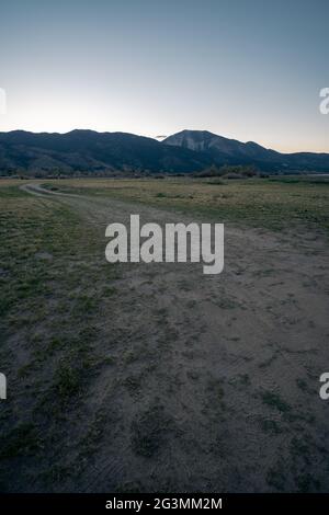 Vista naturale di una strada sterrata in primo piano che conduce verso la montagna durante l'ora blu Foto Stock