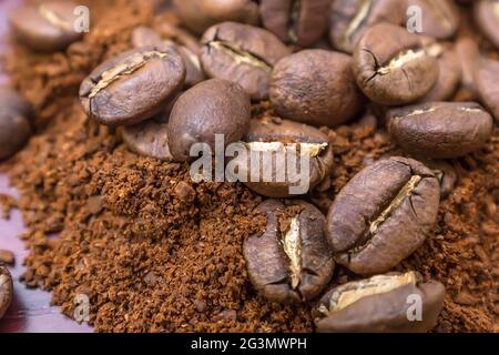 I chicchi di caffè arrosto si trovano sopra un mucchio di caffè macinato Foto Stock