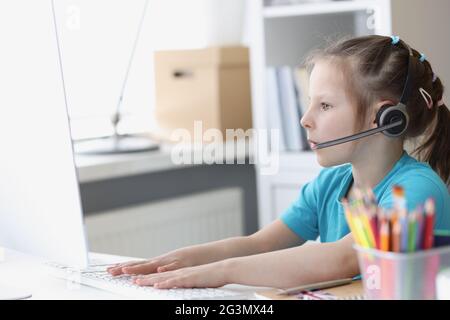 La bambina al computer in cuffie con microfono funziona al computer. Foto Stock