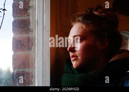 '03.04.2021, Briescht, Brandeburgo, Germania - giovane donna che guarda attentamente fuori da una finestra. 00S210403D629CAROEX.JPG [RELEASE DEL MODELLO: SÌ, PROPRIETÀ Foto Stock