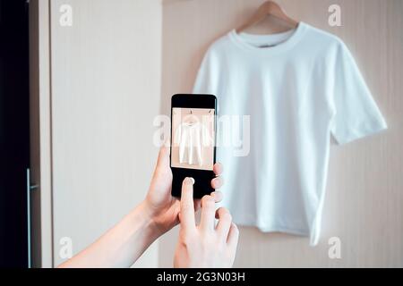 La donna sta scattando una foto su uno smartphone di abbigliamento usato per la rivendita o la carità Foto Stock