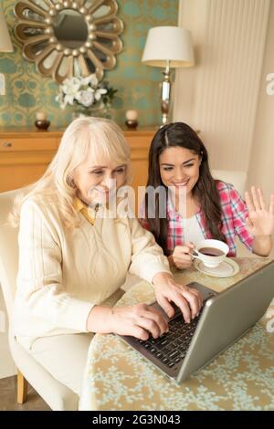 Donna anziana allegra tipi sul portatile seduto accanto alla a figlia Foto Stock