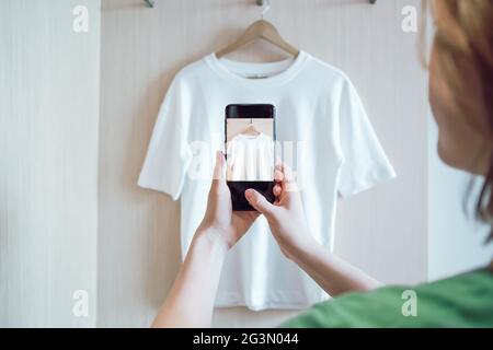 La donna sta scattando una foto su uno smartphone di abbigliamento usato per la rivendita o la carità Foto Stock