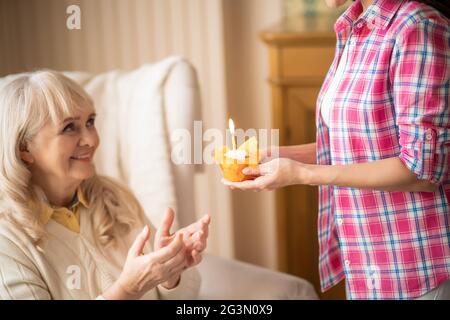 La figlia affascinante dà la piccola cupcake di compleanno con la candela alla sua madre più anziana Foto Stock