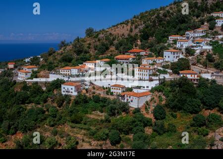 Vuno, Albania - 7 agosto 2020: Vista del paese - tradizionali case bianche con tetti arancioni e persiane in legno su finestre - sulla collina di montagna Foto Stock