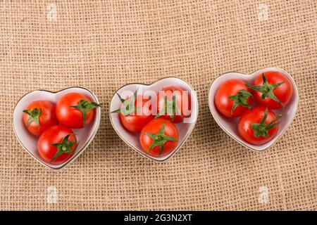 Tomatos di ciliegio rosso in ciotola a forma di cuore Foto Stock