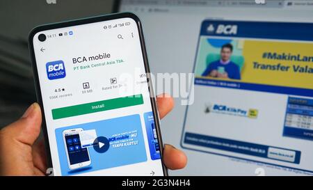Dumai, indonesia - Giugno 17,2021: La mano dell'uomo asiatico sta tenendo un telefono cellulare e aprendo l'app BCA, con sfondo laptop Foto Stock