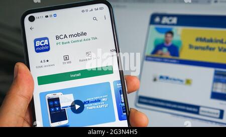 Dumai, indonesia - Giugno 17,2021: La mano dell'uomo asiatico sta tenendo un telefono cellulare e aprendo l'app BCA, con sfondo laptop Foto Stock