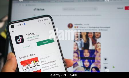 Dumai, indonesia - Giugno 17,2021: La mano dell'uomo asiatico sta tenendo un telefono cellulare e sta aprendo l'app TIKTOK, con sfondo laptop Foto Stock