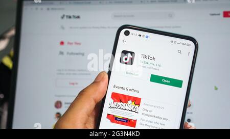 Dumai, indonesia - Giugno 17,2021: La mano dell'uomo asiatico sta tenendo un telefono cellulare e sta aprendo l'app TIKTOK, con sfondo laptop Foto Stock