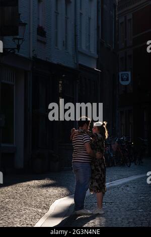 La ragazza abbraccia il suo ragazzo in una strada acciottolata. Foto scura in controluce, i capelli della coppia in amore si illuminano lungo il bordo della testa Foto Stock