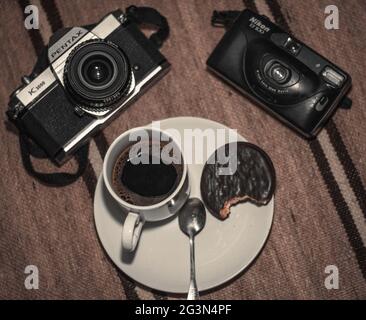 Un mazzo di vecchie macchine fotografiche mostrate splendidamente con una tazza di caffè e alcuni dolci, Pentax K1000, Camera Vintage. Foto Stock