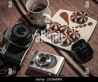 Un mazzo di vecchie macchine fotografiche mostrate splendidamente con una tazza di caffè e alcuni dolci, Pentax K1000, Camera Vintage. Foto Stock