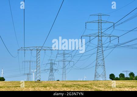 Piloni elettrici e linee elettriche con turbine eoliche in background Foto Stock