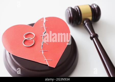 Due anelli d'oro giacenti sul cuore di carta rosso vicino al closeup del martello del giudice Foto Stock