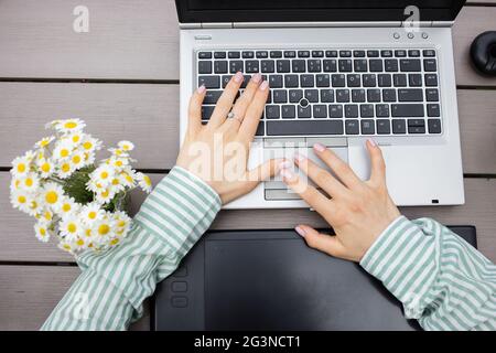 tastiera grigia per computer portatile, tablet grafico nero, bouquet di margherite e mani femminili in una camicia a righe. ufficio, donna d'affari, designer, studente, modera Foto Stock