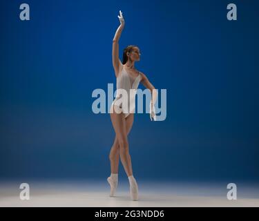 Sulle punte delle dita dei piedi. Giovane ballerina bella in azione isolata su sfondo blu. Foto Stock