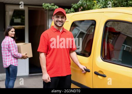 Sorridente delivery guy standing vicino a giallo van. Foto Stock