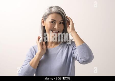 Sorridente donna asiatica tocca i suoi capelli grigi Foto Stock