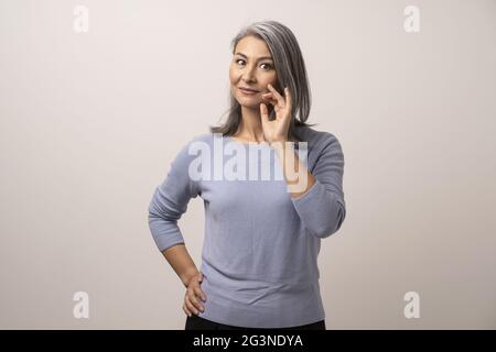 Sorridente donna asiatica tocca i suoi capelli grigi Foto Stock