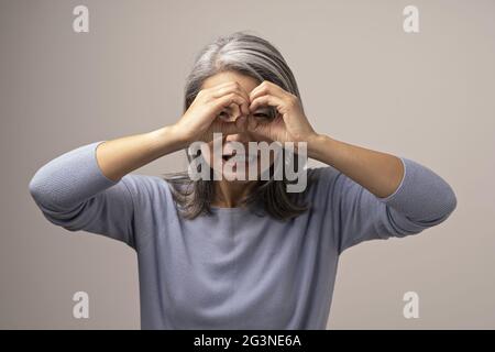 Asian donna matura non ok gesto come un binocolo. Foto Stock