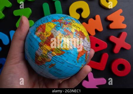 Mano che tiene un modello globo su lettere colorate su uno sfondo nero Foto Stock