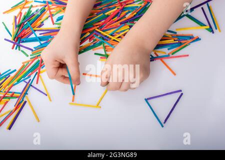 Capretto che fa le forme geometriche con i bastoncini colorati su sfondo bianco Foto Stock
