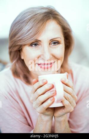 Donna matura felice con tazza di tes nelle sue mani Foto Stock