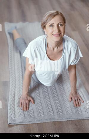 La donna matura si alza in posa del cane rivolta verso l'alto Foto Stock