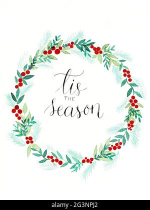 Illustrazione della corona di Natale con agrifoglio e conifere fatto come un dipinto acquerello con calligrafia 'tis la stagione' all'interno Foto Stock