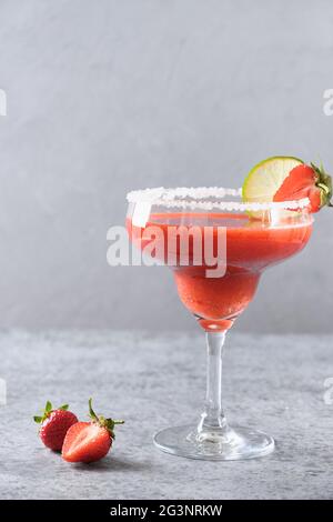 Cocktail Margarita alla fragola o frullato che guarnisce il lime su uno sfondo grigio. Orientamento verticale. Bevanda alcolica estiva fresca. Primo piano. Foto Stock