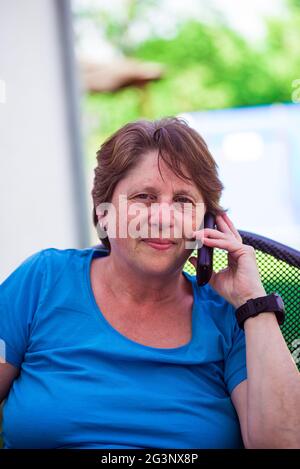 Una donna di mezza età parla con un telefono cordless all'esterno. Foto Stock