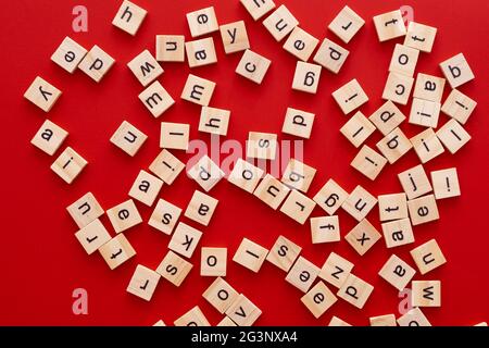 Immagine di sfondo le lettere sono sparse in disordine. Lettere inglesi. Lettere quadrate di legno su sfondo rosso brillante. Biglietto d'auguri, pronto all'uso Foto Stock