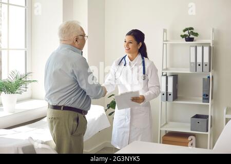 Paziente anziano maschile e medico donna agitando a mano presso il moderno studio clinico Foto Stock