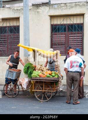 Un uomo che vende verdure su un carrello di triciclo a bordo strada Sulla strada mentre la gente guarda le verdure sul carrello Foto Stock