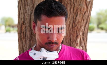 Ritratto di un uomo asiatico che legge un libro in camicia rosa e maschera. Dopo aver bloccato l'uomo seduto contro una corteccia di albero in un giardino. Foto Stock