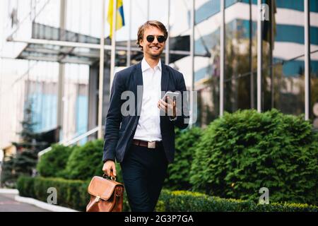 Femmina in un ufficio Suit passeggiate attraverso il quartiere finanziario che porta un sacco e un telefono cellulare Foto Stock