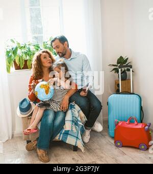 Genitori felici e piccola figlia seduto in poltrona a studiare globo. Foto Stock