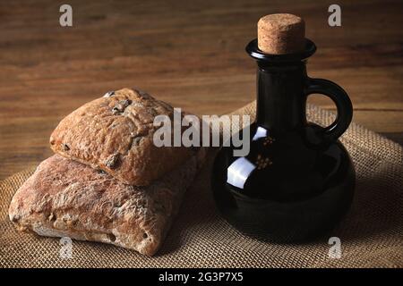 Due focacce di pane e una bottiglia di aceto balsamico in un ambiente rustico. Foto Stock