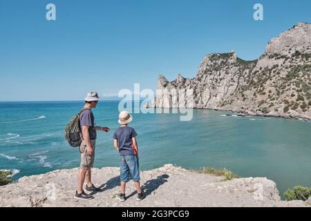 Un ragazzo e suo nonno in piedi sulla riva della baia e guardando la roccia. Concetto di viaggio locale. Foto Stock