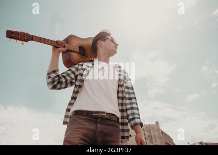 Cute Young Guy Con Una Chitarra Si Leva In Piedi Nel Cielo In Un Giorno D'Estate. Vista Dal Basso. Foto Stock